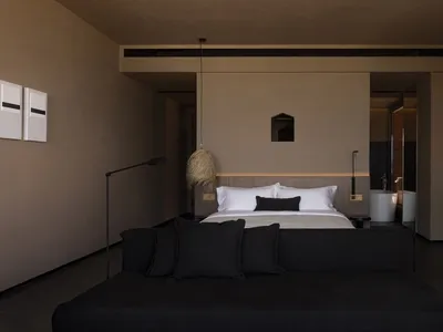 Modern minimalist bedroom featuring a concrete bed platform with leather headboard and wool pillows.