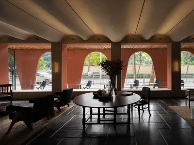 Modern minimalist hotel lounge featuring wooden furniture and leather accents, with a round table, chairs, and vases of flowe
