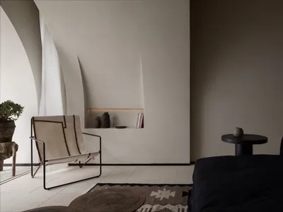 Minimalist living room with concrete walls, a black sofa, and a woven chair.