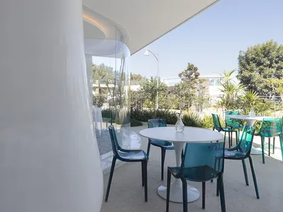 A modern restaurant terrace with glass walls, concrete surroundings, and metal chairs and tables.