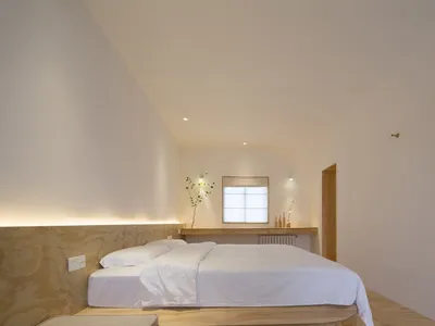 Minimalist bedroom with a white bed, wooden headboard, and minimalist decor.