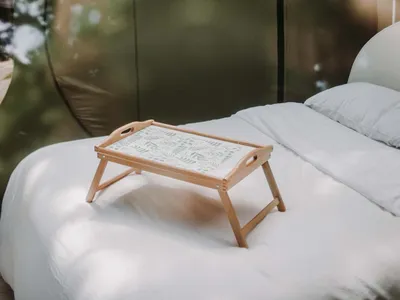 A minimalist bedroom with a white bed and wooden tray on top of it, set against a backdrop of a transparent dome structure vi