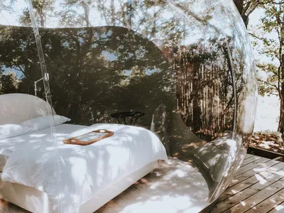 Photograph of a modern bedroom with a clear plastic tent structure and a bed with white bedding.