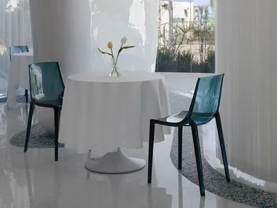 A minimalist restaurant interior with a white tablecloth, glass vase with tulips, and transparent blue plastic chairs.