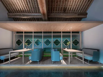 A modern restaurant interior with a wooden floor and ceiling, greenery accents, and blue seating arrangements.