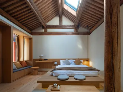 A minimalist bedroom with a wooden bed, light-colored bedding, and a skylight in the ceiling.