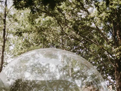 Transparent bubble-shaped outdoor bedroom with a white bed and minimalistic design.