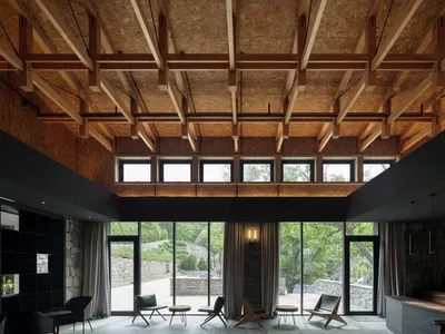 An industrial hotel suite featuring exposed wooden beams, brick walls, and a stone floor, with large windows offering a view