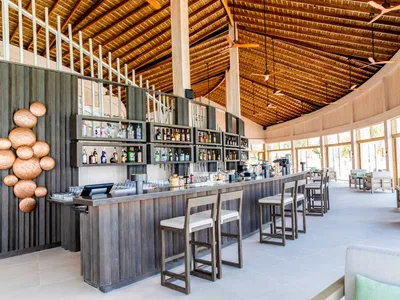 Modern bar interior with wooden ceiling, concrete counter, and seating area.