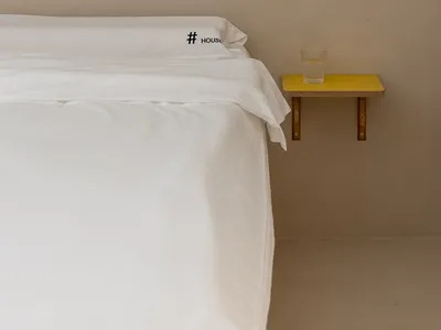 A minimalist bedroom with white textiles on a concrete wall.