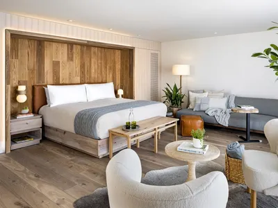 A minimalist hotel suite featuring a wooden bed and furniture.