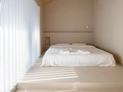 Minimalist bedroom featuring a brown ceiling, concrete floor, and white textiles on the bed.