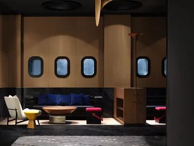 A modern hotel lobby featuring a black leather sofa with blue pillows, a wooden coffee table, and a metal lamp on a wooden fl