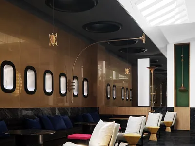A modern hotel lobby features sleek furniture, glass walls, and a high ceiling with skylights.