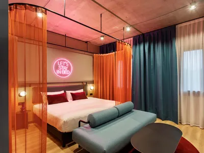 Modern hotel room with a bed, curtains, and a sign that says 'Let's Stay in Bed'.