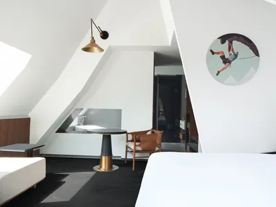 Modern hotel room with white and black color scheme, featuring a contemporary bed, desk, and seating area with a unique hangi