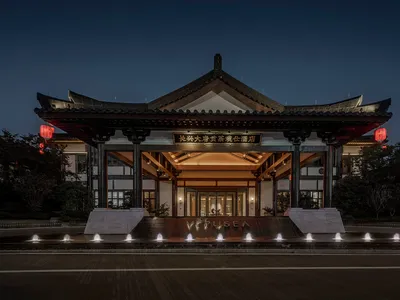 A traditional Chinese hotel entrance with brick and marble columns, illuminated by lanterns and modern lighting.