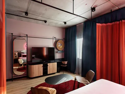 A modern minimalist hotel bedroom suite featuring a large bed, a flat-screen TV, and a comfortable seating area with wooden f