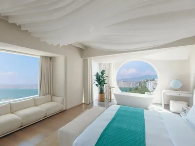 Modern minimalist hotel room with white decor and a view of the ocean.