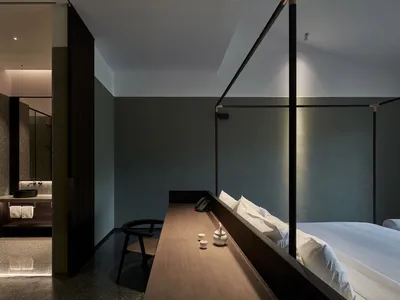 A modern bedroom with dark interior design features a wooden desk, a metal canopy bed, and a minimalist design aesthetic.