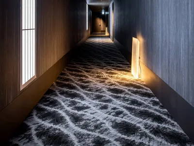 A dark minimalistic hotel hallway with metallic walls, textured carpet, and warm lighting at the end.