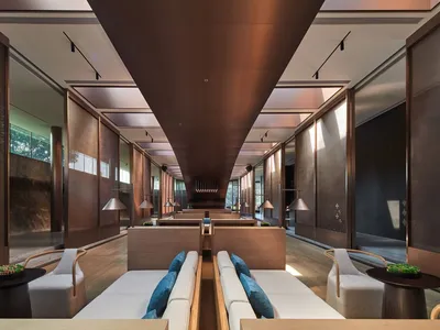 A contemporary hotel lounge area with wooden furniture, concrete flooring, and decorative room dividers.