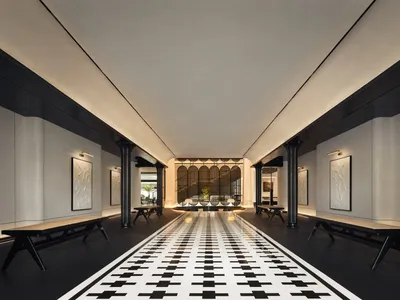 A modern hotel lobby with concrete walls, black sand floor tiles, and a long black and white checkered floor leading to a sea