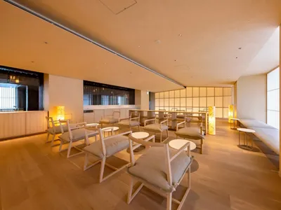 Interior of a modern restaurant with wooden flooring, cushioned chairs, and warm lighting.