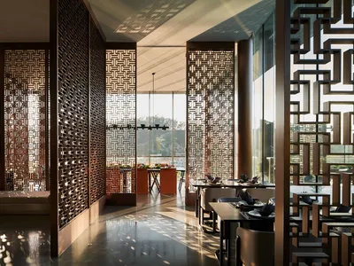 A modern restaurant interior featuring metallic wall screens and wooden tables.