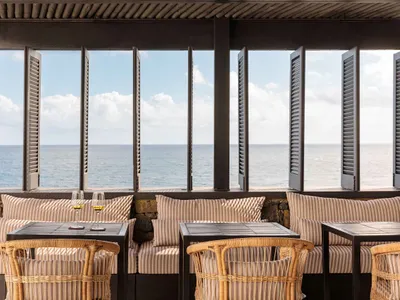 海濱餐廳酒吧享有海景，搭配木質家具、石材點綴與窗簾。兩杯紅酒