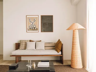 A modern living room featuring a wooden sofa, woven-fiber floor lamp, and abstract wall art.