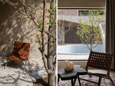 A metal chair and a small table with three candles in a space with a concrete wall and a tree casting shadows on it.