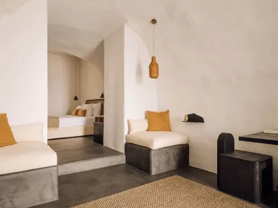 A minimalist bedroom with beige and orange cushions on a concrete bench, and a woven pendant light.
