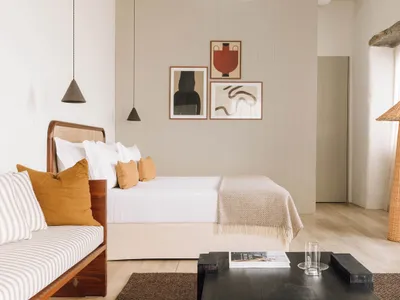 A minimalist bedroom with neutral tones, featuring a bed, modern pendant lights, abstract art, and a rattan floor lamp.