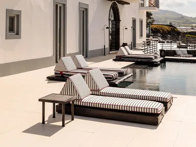 Modern minimalist hotel pool deck featuring concrete flooring, daybeds with striped cushions, and a serene outdoor space.