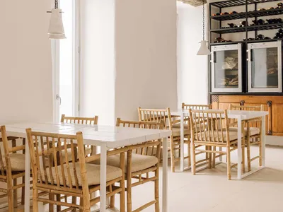 A minimalist restaurant dining room with white walls, wooden tables and chairs, and hanging stone decor.