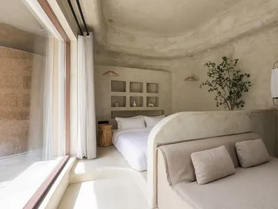 A minimalist bedroom with concrete walls, a large bed, and a grey sofa.