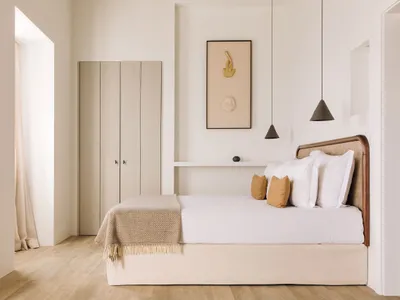 A modern minimalist bedroom featuring a bed with a wooden headboard, white bedding, and wooden flooring.