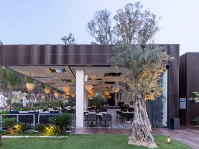 A modern outdoor restaurant with wooden panels, trees, and large windows overlooking a natural landscape.