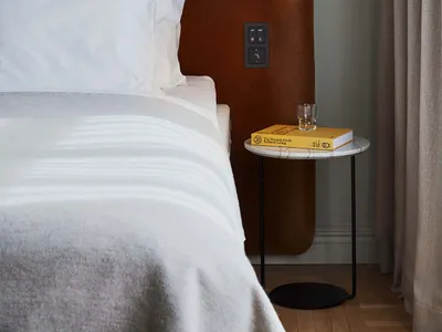A minimalist bedroom with a brown upholstered headboard, white bedding, and a small marble side table.