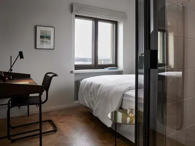 A minimalist bedroom with a white bed, a desk, and a glass door.