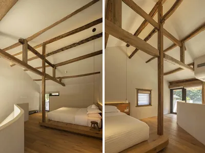 Modern minimalist bedroom with exposed wooden beams, white walls, and a bed on a wooden frame.
