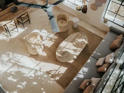 Modern minimalist living room with concrete walls and floor, featuring a grey sofa, wooden coffee table, and natural fiber pe
