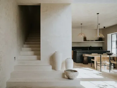 A minimalist kitchen with concrete elements, featuring a dining table and pendant lights.
