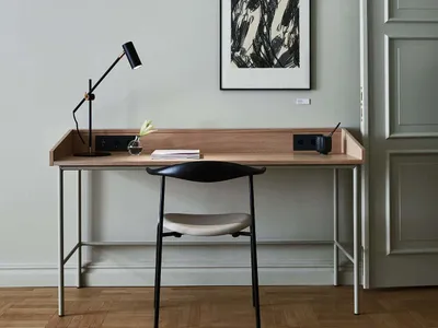A minimalist home office featuring a wooden desk with metal legs, a black table lamp, and a black and white abstract artwork