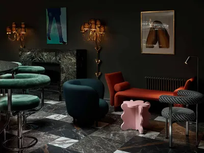A modern lounge interior featuring comfortable seating, a fireplace, and stylish lighting against a dark, marble floor backgr