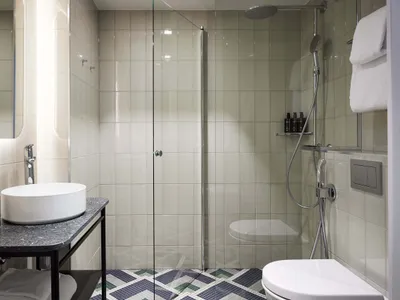 Modern, minimalist bathroom featuring tile, concrete, patterned flooring, steel shower faucet, and glass shower door.