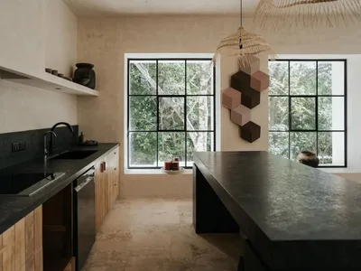 Modern minimalist kitchen with black countertops on concrete floor and large windows looking out to greenery.