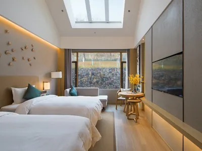 A modern minimalist bedroom with neutral-toned walls and furniture, featuring two twin beds, a double-height ceiling with a s