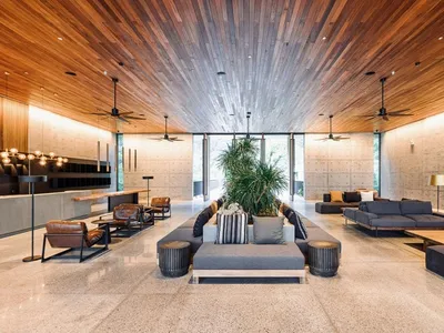A spacious, modern industrial hotel lobby featuring concrete walls, a high wooden ceiling, comfortable seating areas, and a c